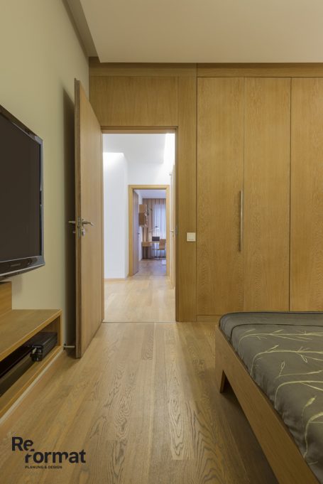 Schlafzimmer mit Holzfußboden, TV und offener Tür zu einem anderen Raum.