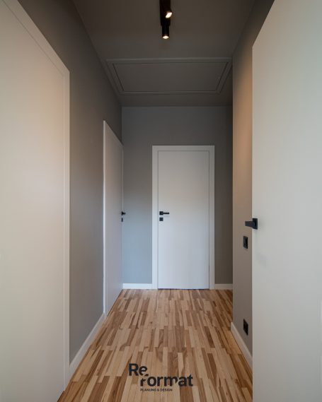 Langer Flur mit grauen Wänden, hellen Türen und Holzfußboden.